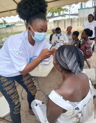 A field researcher in Ghana holds a smartphone up to capture an image of a participant's eye